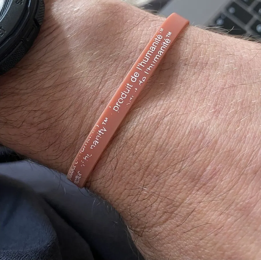 Rosa Silikonarmband mit weißem Aufdruck „product of humanity™“ an einem Handgelenk